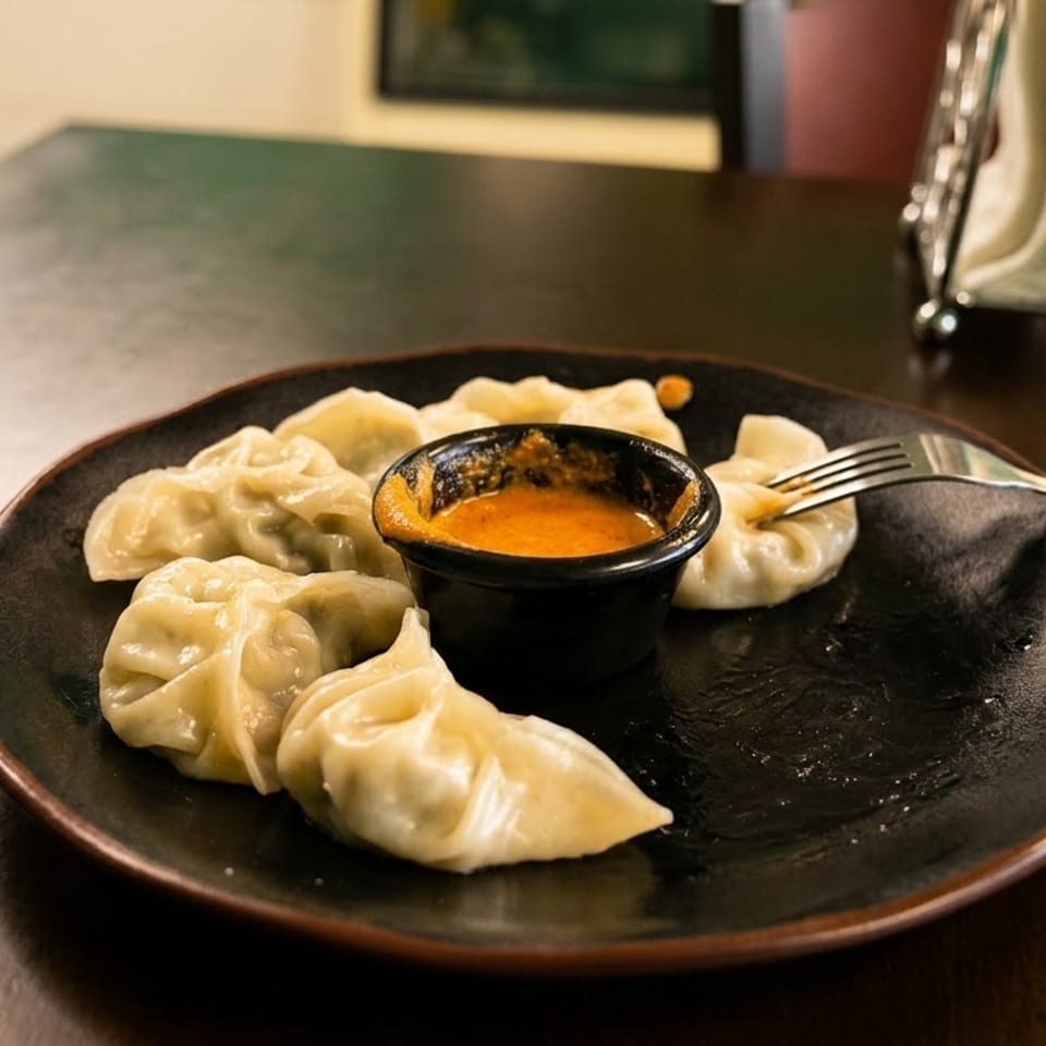 A plate of steamed dumplings with a small bowl of orange dipping sauce and a fork.