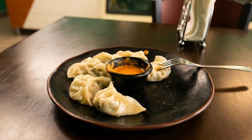 A plate of steamed dumplings with a small bowl of orange dipping sauce and a fork.