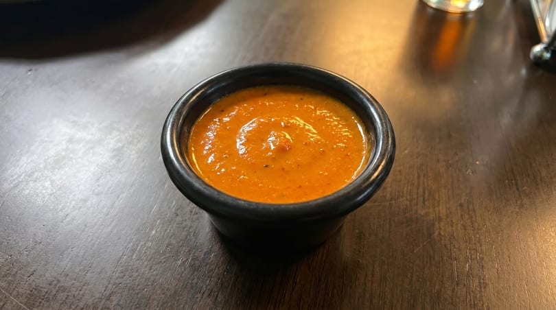 A small black ramekin filled with vibrant orange salsa, resting on a dark wooden table.